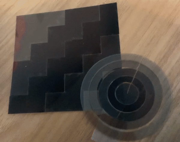 concentric circles on the bottom right and a square in the top left made of polarizers (tinted plastic). the concentric circles ripple in different gradients. the square ripples diagonally from one corner to the opposite corner.