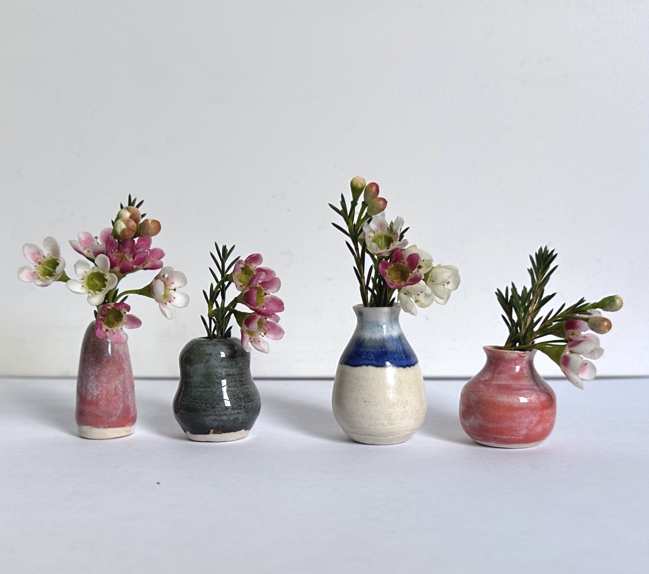 4 miniature pots with flowers in a row